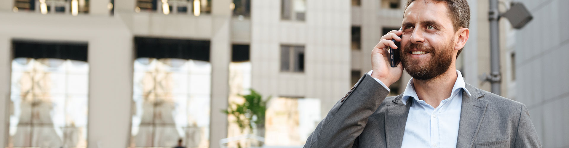 Seguros Banca Privada - Hombre de negocios con un traje gris y camisa blanca hablando por el móvil junto a un edificio en una ciudad