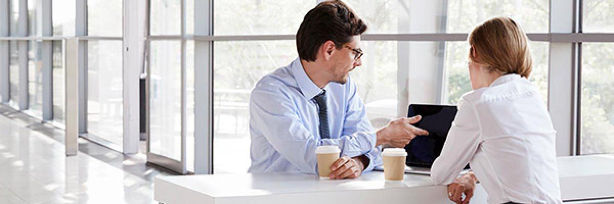 Financiación preferente - Reunión de negocios entre un hombre y una mujer de negocios con camisa, frente a un portátil hablando y tomando café